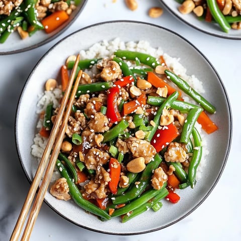 A vibrant plate of stir fry with chicken, green beans, and veggies served alongside chopsticks.